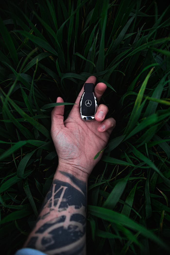 mobile-02 Close-up of a tattooed hand holding a luxury car key surrounded by lush green leaves.