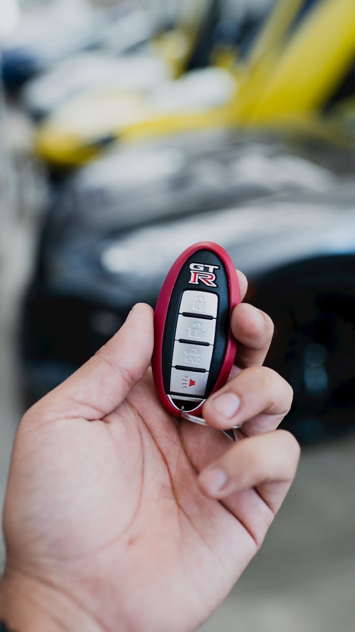 creative-02 A hand holding a sporty Nissan GT-R key fob with blurred luxury cars in the background.
