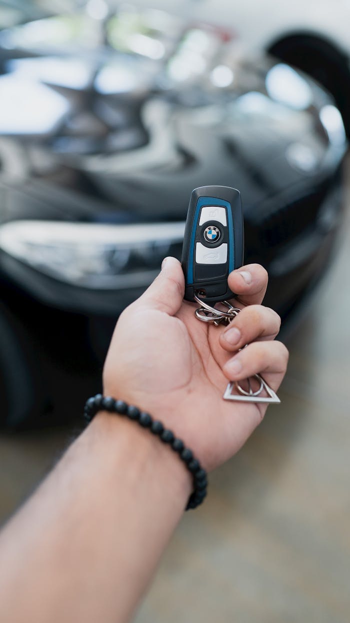 Home Close-up of a hand holding a luxury car key in focus, with the vehicle blurred in the background.